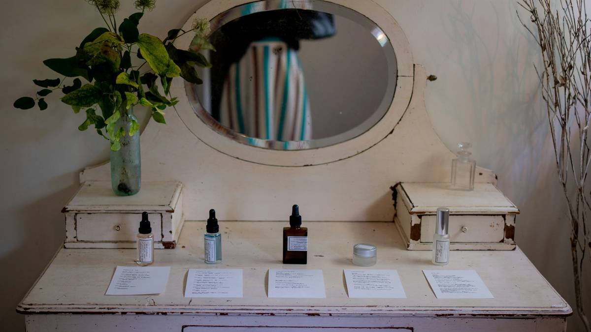 woman applying clean and clear skin care routine products with minimalist glass bottles on wooden countertop